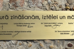 Liela izmēra misiņa plāksne ar gravētu tekstu. Gravējums ir krāsots melnā krāsā.